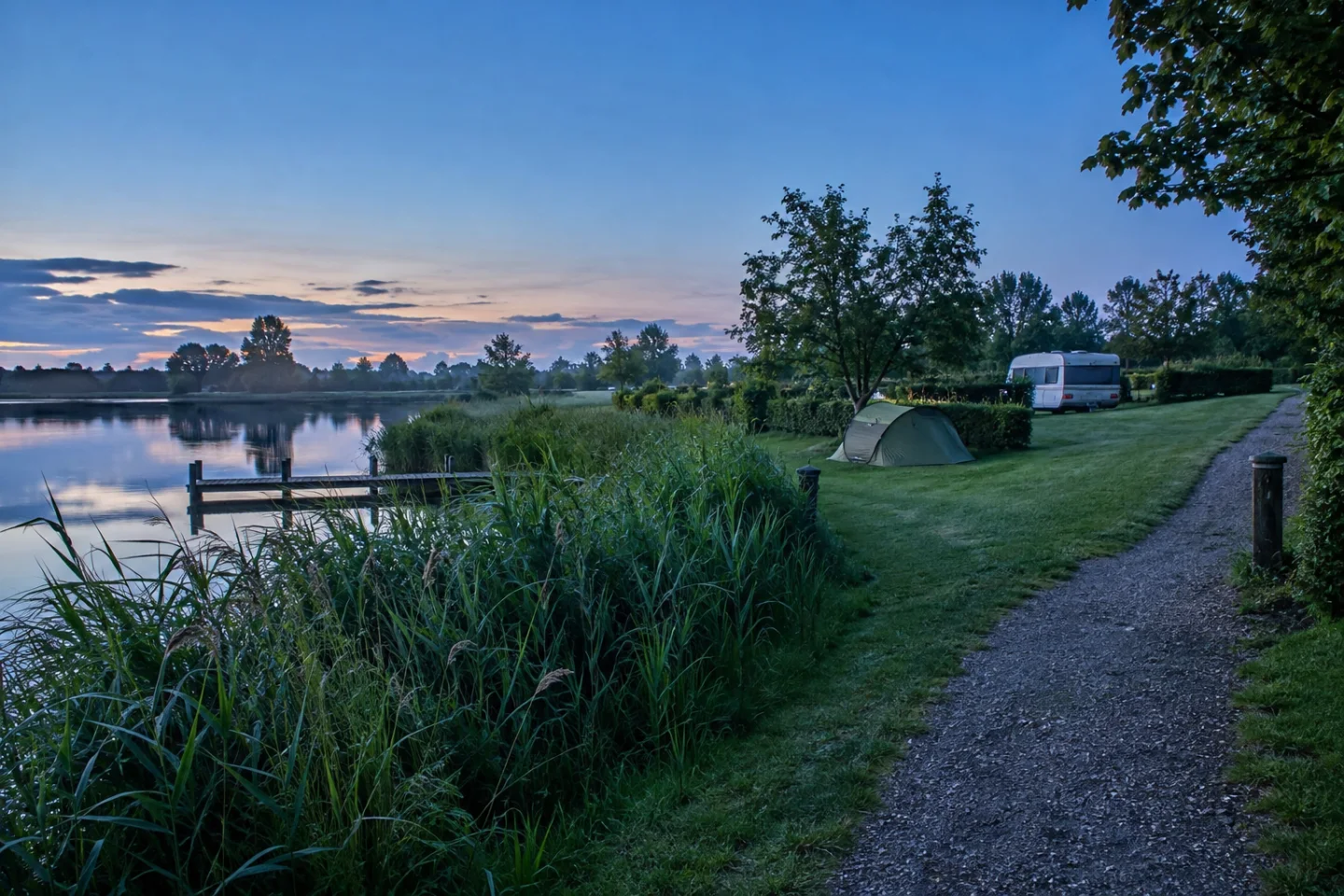 Kampeerplaatsen met een tent en caravan aan het water in zacht ochtendlicht.